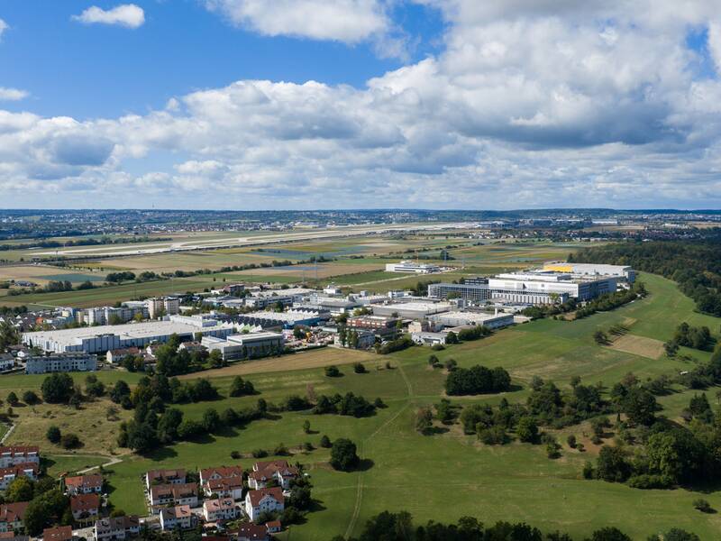 Die Luftaufnahme zeigt eine weitläufige Landschaft mit einem Industriegebiet, Wohnhäusern und Feldern unter einem bewölkten Himmel.