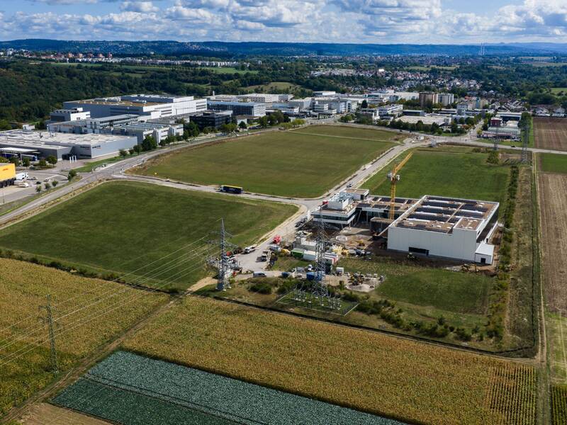 Luftaufnahme einer weitläufigen Landschaft mit einem Industrie- und Logistikpark, umgeben von Feldern und Wiesen.